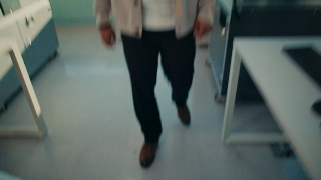 Video Reference: person, walking, indoor, blurred, motion blur, room, corridor, tables, counters, office, laboratory, interior, lower body, legs, casual clothes