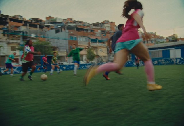 Video Reference: soccer, football, sports, players, outdoor field, action, running, ball, community, urban, hillside, colorful uniforms, competition, motion blur