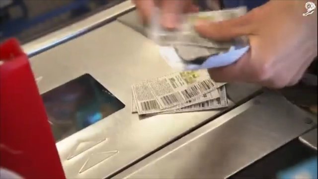 Video Reference: close-up, hands, ticket, receipt, scanner, checkout, transit, gate, barcode, paper, machine, payment, transaction, indoor, metal, blurred