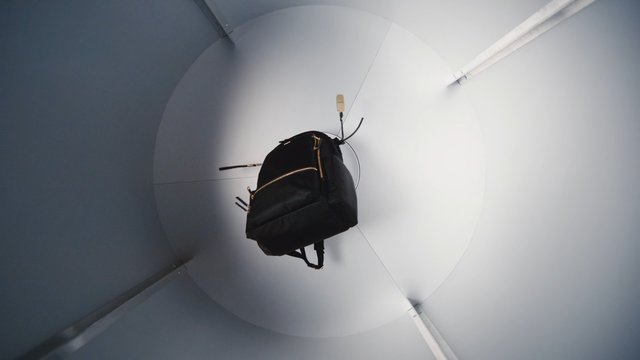 Video Reference: backpack, hanging object, product display, white background, minimalist, indoor, studio lighting, fashion accessory, bag, suspended, curved wall, centered, modern, clean background