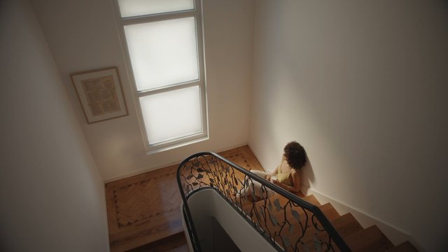 Video Reference: interior, staircase, woman, window, hallway, home, wooden floor, natural light, sitting, indoor, architecture, minimal, residential, stairs