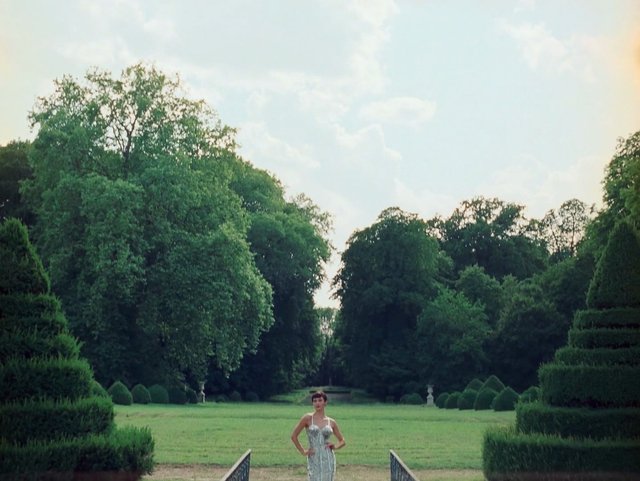 Video Reference: garden, woman, path, trees, hedges, lawn, outdoors, formal garden, greenery, sky, landscape, park, standing, summer, nature