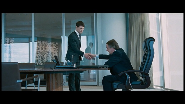 Video Reference: Sitting, White-collar worker, Conversation, Gentleman, Screenshot, Suit, Scene, Photography, Furniture, Person, Man, Indoor, Window, Front, Looking, Computer, Table, Laptop, Small, Young, Desk, Office, Standing, Room, Woman, Holding, People, White, Phone, Clothing, Chair, Text