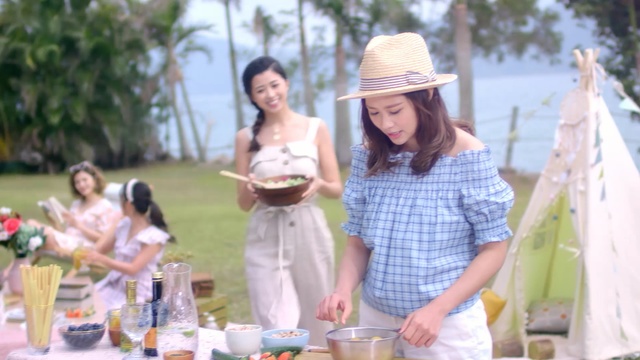 Video Reference: Picnic, Recreation, Event, Fashion, Summer, Headgear, Party, Fashion accessory, Dress, Brunch, Person, Outdoor, Table, Woman, Standing, Man, People, Food, Holding, Group, Water, Girl, Young, Talking, Park, Cake, Boat, Plate, White, Tree, Clothing, Hat, Sun hat, Human face, Smile, Bottle