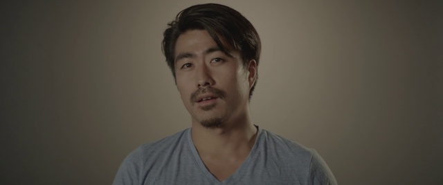 Video Reference: Hair, Face, Facial hair, Chin, Forehead, Cheek, Beard, Eyebrow, Moustache, Nose, Person, Man, Indoor, Shirt, Looking, Front, Holding, Standing, Young, Video, Camera, Remote, Glasses, Wearing, Smiling, Hand, Game, Wii, Room, Living, Playing, White, Wall, Human face, Portrait, Clothing, Human beard, Headshot, Jaw, Neck, Pointing, Male