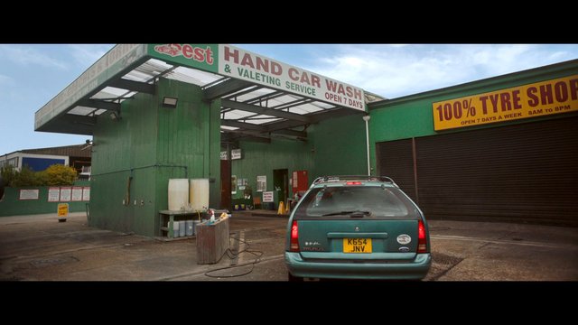 Video Reference: car wash, tyre shop, auto service, station wagon, parked car, industrial building, outdoor, commercial, garage, signage, wet pavement, daytime, green building, repair shop