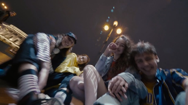 Video Reference: Social group, Fun, Event, Crowd, Person, Man, People, Sitting, Young, Holding, Table, Boy, Riding, Woman, Room, Group, Standing, White, Playing, Street, Phone, Human face, Clothing, Smile
