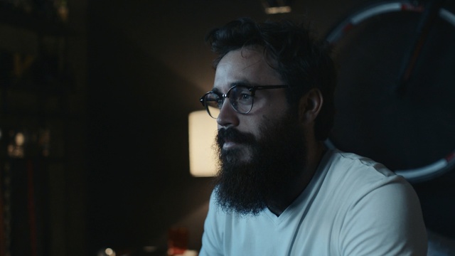 Video Reference: Facial hair, Hair, Beard, Glasses, Chin, Audio equipment, Forehead, Microphone, Moustache, Eyewear, Person, Man, Indoor, Looking, Holding, Shirt, Front, Sitting, Standing, Wearing, Food, Hand, White, Laptop, Computer, Room, Table, Game, Video, Young, Remote, Pizza, Human face, Human beard, Clothing, Portrait, Face
