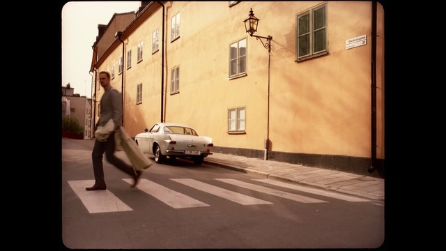 Video Reference: Vehicle, Car, Snapshot, Mode of transport, Photography, Street, Road, Compact car, Asphalt, Building, Outdoor, Man, Front, Light, Parked, Yellow, Sitting, Traffic, Walking, Woman, City, Sign, Standing, Side, Intersection, Riding, Board, Red, White, Clock, Snow, Land vehicle, Text, Wheel, Window