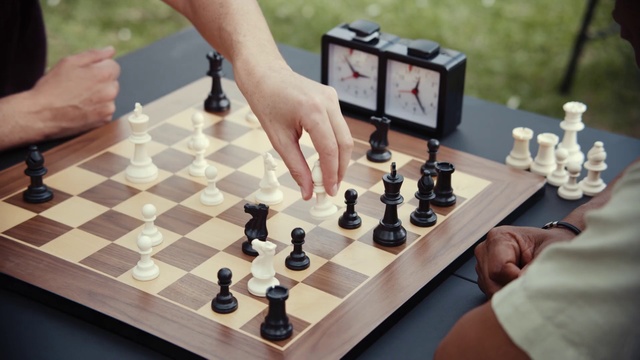 Video Reference: Indoor games and sports, Board game, Chessboard, Games, Chess, Recreation, Tabletop game, Play, Table, Hand, Person, Object, Thing, Man, Indoor, Sitting, Food, Wine, Small, Woman, Holding, Plate, Glass, Laptop, Wooden, Cake, Birthday, People, Computer, Eating, White, Standing, Sports equipment, Chessman, Gambling, Card game, Poker, Casino, Poker table