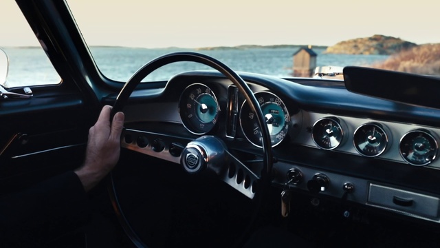 Video Reference: Land vehicle, Vehicle, Car, Steering wheel, Steering part, Classic car, Center console, Sedan, Coupé, Window, Front, Dog, Mirror, Looking, Small, View, Side, Sitting, Man, Holding, Water, Parked, Woman, Riding, Automotive, Auto part, Wheel, Speedometer, Control panel, Vehicle door