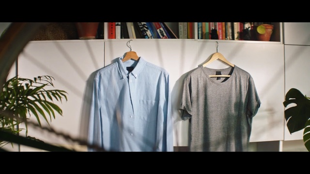 Video Reference: Clothing, White, T-shirt, Shirt, Clothes hanger, Sleeve, Dress shirt, Fashion, Outerwear, Formal wear, Indoor, Man, Window, Photo, Table, Front, Standing, Room, Hanging, Screen, Kitchen, Television, Mirror, Holding, Glass, Closet, Text, Coat