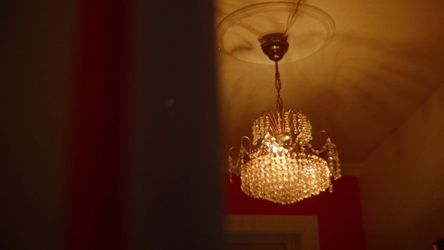 Video Reference: Light fixture, Lighting, Light, Chandelier, Lighting accessory, Ceiling fixture, Incandescent light bulb, Ceiling, Interior design, Lamp, Person, Indoor, Object, Thing, Table, Sitting, Wine, Lit, Glasses, Red, Front, Looking, Glass, Dark, Room, Mirror, White, Reflection, Man, Cat, Holding, Standing, Lantern, Candle, Light bulb, Fashion accessory, Gold
