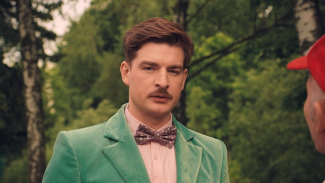 Video Reference: green, gentleman, tree, human, outerwear, plant, suit, smile, formal wear, grass, Person