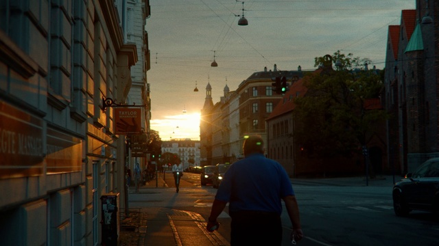 Video Reference: Sky, Street, Urban area, Town, Neighbourhood, Evening, Morning, Light, Road, Snapshot, Person, Outdoor, Building, Man, Sidewalk, City, Walking, Cross, Traffic, Standing, Side, Corner, Red, Yellow, Fire, Hydrant, Stop, Riding, Woman, Street light, Text, Way