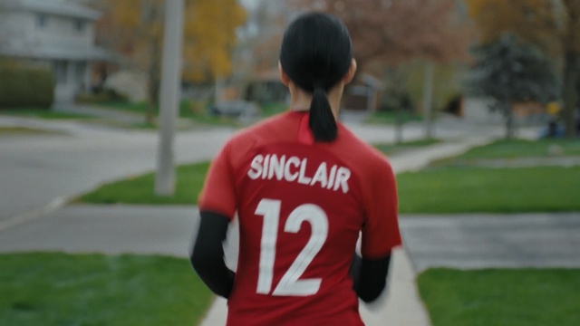 Video Reference: Red, Player, Sportswear, Grass, Jersey, T-shirt, Team, Team sport, Shoulder, Football player, Person, Outdoor, Baseball, Building, Game, Uniform, Holding, Standing, Young, Field, Walking, Ball, Wearing, Soccer, Green, Man, Bat, Clothing, Sports uniform, Human face