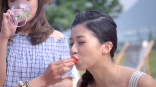 Video Reference: Lip, Nose, Skin, Water, Mouth, Eating, Summer, Neck, Drinking, Vacation, Person, Outdoor, Woman, Wine, Food, Glasses, Girl, Table, Sitting, Holding, Glass, People, Young, Standing, White, Man, Teeth, Plate, Group, Human face, Food craving, Dessert