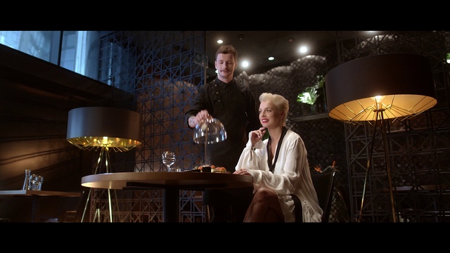Video Reference: Gentleman, Event, Fun, Performance, Photography, Flash photography, Scene, Stage, Darkness, Person, Man, Indoor, Table, Front, Standing, Holding, Glasses, Wearing, Wine, Woman, Large, Suit, Room, Young, Shirt, White, Clothing, Human face, Smile, Furniture