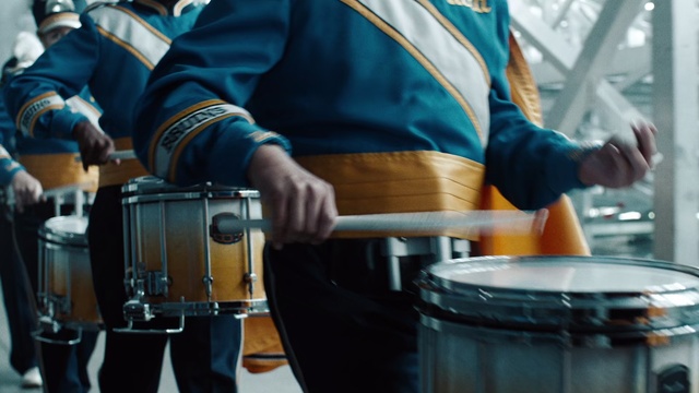 Video Reference: Drum, Percussionist, Musician, Musical instrument, Percussion, Snare drum, Repinique, Tom-tom drum, Drumhead, Marching percussion, Person, Table, Food, Man, Holding, Kitchen, Woman, Standing, Young, Wearing, Cooking, Shirt, Eating, People, Plate, Stove, Pan, Blue, Music, Clothing, Band, Membranophone, Jazz, Waste container