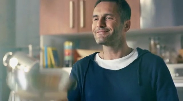 Video Reference: Facial expression, Chin, Smile, Jaw, Photography, Neck, Happy, Person, Building, Indoor, Man, Kitchen, Holding, Table, Looking, Standing, Front, Food, Blue, Woman, Shirt, Young, Smiling, Black, Pizza, Plate, Restaurant, Phone, Human face, Clothing