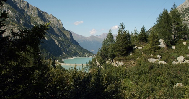 Video Reference: Mountainous landforms, Mountain, Nature, Body of water, Natural landscape, Wilderness, Highland, Tarn, Mountain range, Lake, Person, Outdoor, Grazing, Grass, Field, Background, Hillside, Green, Sheep, Water, Hill, Tree, Large, Standing, Covered, Herd, Snow, View, Eating, Forest, Group, Horse, Grassy, Flock, Tall, White, River, Man, Sky, Cloud, Landscape, Lush, Surrounded, Distance