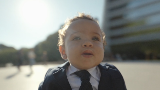 Video Reference: Face, Child, Facial expression, Head, Nose, Cheek, Skin, Male, Chin, Standing, Person, Necktie, Wearing, Young, Boy, Smiling, Small, Suit, Little, Front, Shirt, Man, Dressed, Posing, White, Holding, Red, Water, Blue, Human face, Toddler, Baby, Clothing