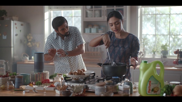 Video Reference: Cooking, Food, Meal, Drink, Person, Indoor, Window, Table, Woman, Kitchen, Man, Looking, Front, Standing, Counter, Glasses, Sitting, People, Holding, Young, Restaurant, Plate, Tableware, Kitchen appliance, Clothing, Bowl, Wok, Cookware and bakeware, Mixing bowl, Home appliance, Dining table