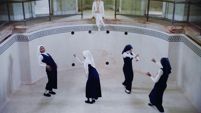 Video Reference: Event, Recreation, Sport venue, Dance, Person, Building, Indoor, Child, Man, Small, Little, Young, Boy, Walking, Front, Standing, Holding, Woman, Suitcase, Bear, Group, Luggage, Riding, People, Playing, Room, Stuffed, Floor, Ground, Clothing