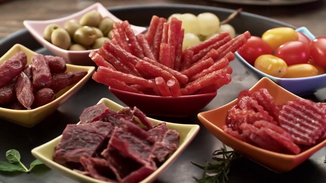 Video Reference: Dish, Food, Cuisine, Red meat, Ingredient, Meat, Salumi, Beef, Charcuterie, Cold cut, Table, Plate, Indoor, Bowl, Sitting, Fruit, Filled, Black, Small, Brown, Various, Different, Holding, Wooden, Banana, Pasta, Toppings, Fast food, Delicious, Healthy, Tomato, Salami, Containing, Vegetable