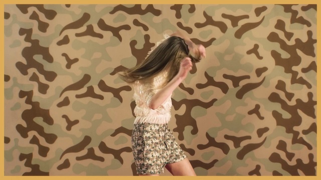 Video Reference: Dress, Pattern, Long hair, Design, Room, Textile, Wallpaper, Visual arts, Fawn, Person, Shirt, Man, Sitting, Young, Yellow, Wearing, Woman, Holding, Standing, Phone, Text, Clothing, Girl, Human face