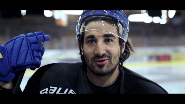 Video Reference: Sports gear, Ice hockey, Hockey protective equipment, Hockey, Personal protective equipment, Stick and ball games, Facial hair, Team sport, Beard, Player, Person, Man, Indoor, Looking, Front, Wearing, Uniform, Computer, Holding, Laptop, Baseball, Sitting, Hat, Black, Standing, Large, Table, Young, Ball, Red, White, Board, Helmet, Human face, Clothing, Sports equipment, Ice skating