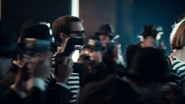 Video Reference: Eyewear, Fashion, Crowd, Performance, Event, Audience, Photography, Glasses, Darkness, Music, Person, Man, Indoor, Cellphone, Phone, Looking, Wine, Sitting, Front, Holding, People, Table, Glass, Room, Drinking, Talking, Woman, Shirt, Standing, Wearing, Group, Young, Human face, Clothing, Camera, Concert band