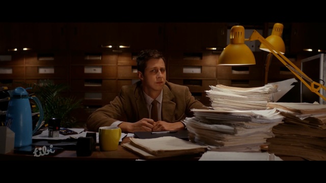 Video Reference: man, bookkeeping, lamp, paper, lot of paper, table, Person
