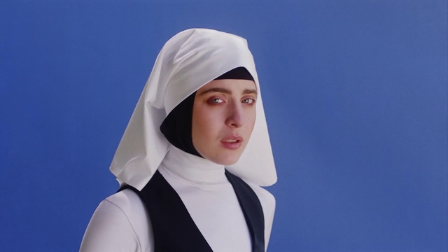 Video Reference: White, Head, Abbess, Headgear, Person, Clothing, Wearing, Shirt, Young, Racket, Man, Posing, Looking, Black, Holding, Standing, Blue, Hat, Woman, Dressed, Player, Human face, Fashion accessory, Scarf, Hijab