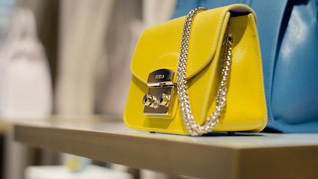 Video Reference: Yellow, Bag, Handbag, Fashion accessory, Fashion, Material property, Luggage and bags, Satchel, Coin purse, Indoor, Table, Sitting, Small, Cellphone, Phone, Food, Holding, White, Man, Standing, Blue, Sandal