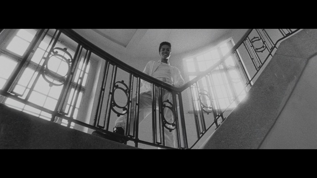 Video Reference: White, Photograph, Black, Monochrome, Black-and-white, Monochrome photography, Iron, Stairs, Snapshot, Handrail, Indoor, Man, Photo, Building, Room, Large, Holding, Screen, Riding, Bed, Table, Standing, Display, Clock, Living, Doing, Bedroom, Black and white, Person, Clothing