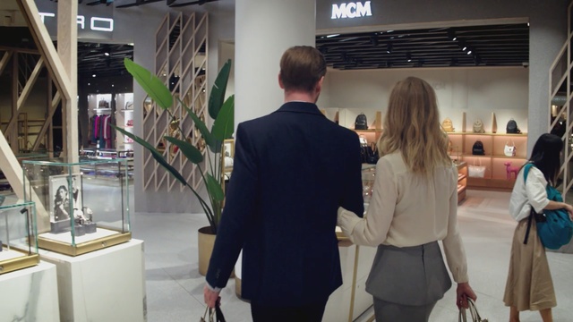 Video Reference: Fashion, Event, Boutique, Interior design, Display window, Person, Standing, Man, Woman, Front, People, Table, Suit, Young, Black, Group, Dressed, Walking, Holding, Wearing, Kitchen, Talking, Wine, Room, Display, Luggage, White, Clothing