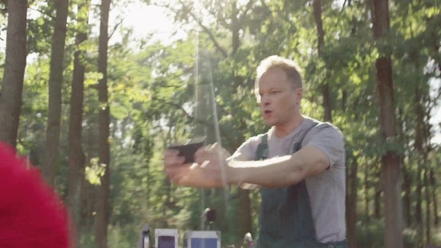 Video Reference: Woodland, Forest, Natural environment, Jungle, Tree, Fun, Recreation, Photography, Wildlife, Firearm, Person, Outdoor, Holding, Man, Standing, Shirt, Hand, Woman, Young, Park, Front, Wearing, Frisbee, Red, Glasses, Table, Pizza, Hat, Food, White, Clothing, Human face
