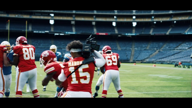 Video Reference: Player, Gridiron football, Sports, Sports gear, American football, Tournament, Sport venue, Canadian football, Sports equipment, Team sport, Person, Building, Grass, Game, Baseball, Ball, Playing, Field, Holding, Team, Group, Standing, Young, Wearing, Soccer, Red, Man, Walking, Woman, White, Court, Helmet, Football helmet, Football, Sports uniform, Football equipment, Sprint football, Clothing, Eight-man football, Football gear, Super bowl, Six-man football, Jersey, Stadium, Arena football, Personal protective equipment