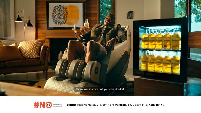 Video Reference: man, living room, massage chair, drink bottle, alcohol, fridge, interior, sofa, lifestyle, home, relaxing, advertisement, beverage, subtitles, responsibility message