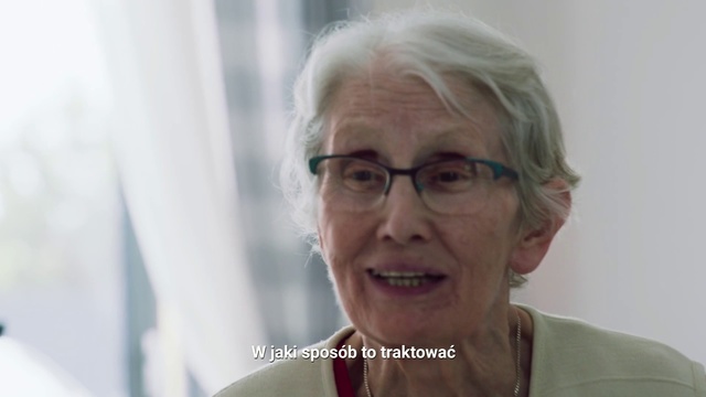 Video Reference: Skin, Wrinkle, Glasses, Grandparent, Smile, Person, Woman, Indoor, Smiling, Holding, Looking, Wearing, Front, Standing, Lady, Man, Sitting, White, Posing, Table, Kitchen, Shirt, Food, Plate, Human face, Portrait