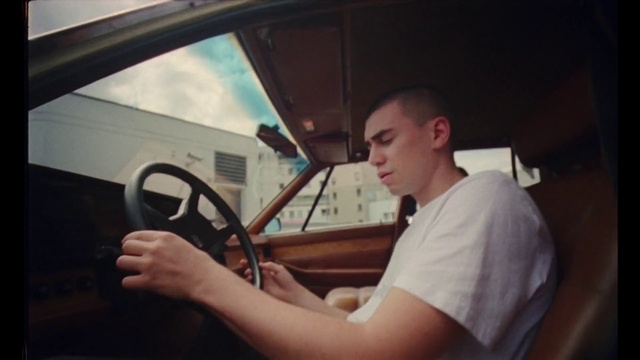 Video Reference: Steering wheel, Steering part, Driving, Vehicle door, Windshield, Vehicle, Car, Automotive design, Automotive window part, Personal luxury car, Person, Indoor, Window, Man, Front, Table, Young, Boy, Sitting, Holding, Standing, Shirt, Woman, Kitchen, Food, White, Mirror, Oven, Land vehicle, Human face, Auto part