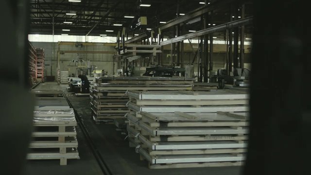 Video Reference: warehouse, factory, industrial, metal sheets, pallets, stacked materials, machinery, workshop, storage, indoor, assembly line, production, steel, large facility, worker