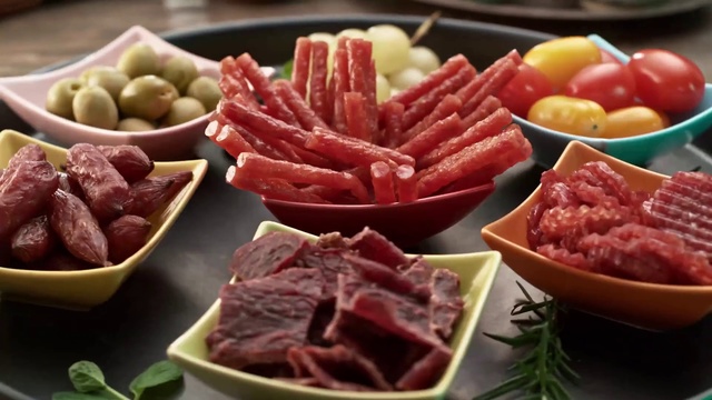 Video Reference: Dish, Food, Cuisine, Red meat, Ingredient, Meat, Salumi, Beef, Charcuterie, Cold cut, Table, Bowl, Plate, Sitting, Fruit, Filled, Couple, Various, Different, Black, Counter, Holding, Wooden, Banana, Brown, Several, Many, Pasta, Delicious, Fast food, Animal fat, Vegetable, Containing