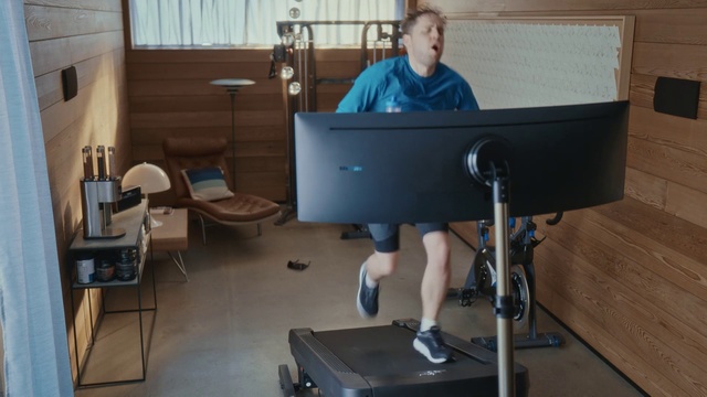 Video Reference: Desk, Standing, Furniture, Exercise machine, Room, Table, Exercise equipment, Electronic instrument, Indoor, Sport, Sitting, Window, Living, Small, Computer, Front, Laptop, Man, Office, Black, Young, Holding, Kitchen, Dog, Mirror, Bed, Blue, White, Sink, Video, Bedroom, Floor, Wall, Exercise device, Chair, Person, Office building, Computer monitor, Television
