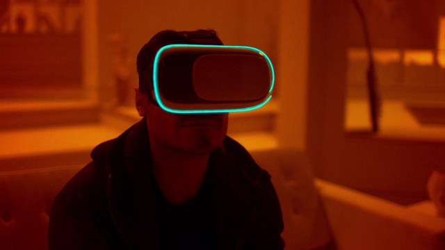 Video Reference: Light, Green, Eyewear, Glasses, Backlighting, Technology, Room, Photography, Neon, Shadow, Person, Indoor, Man, Looking, Sitting, Wearing, Goggles, Front, Camera, Teeth, Holding, Brushing, Sunglasses, Black, Shirt, Mirror, Young, Phone, Seat, Kitchen, Red, White, Hat, Human face, Fashion accessory, Spectacles