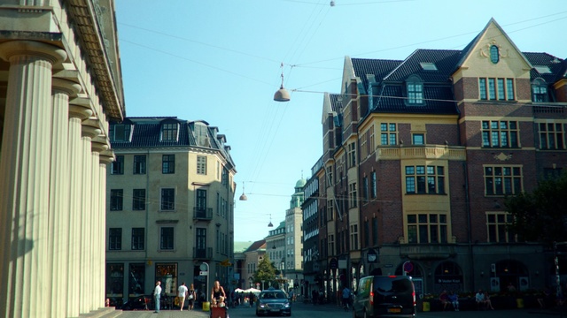 Video Reference: Urban area, Town, Neighbourhood, City, Street, Building, Road, Human settlement, Architecture, Downtown, Outdoor, Intersection, People, Light, Traffic, Sign, Side, Large, Stop, Red, Old, Walking, Man, Tall, Group, Riding, Parked, Standing, White, Clock, Sky, Car, Vehicle, Land vehicle, House, Travel, Text, Government building