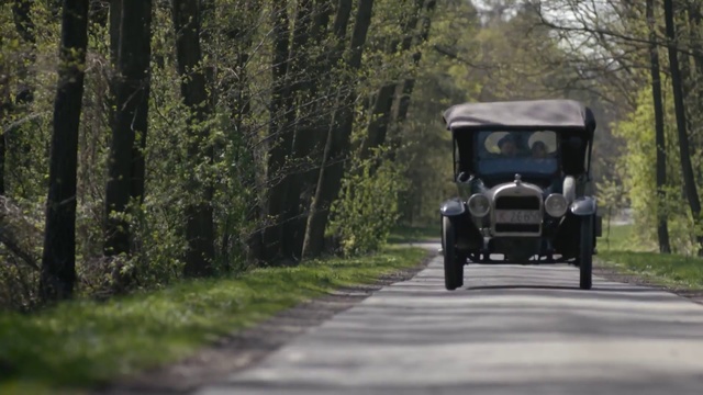 Video Reference: Land vehicle, Vehicle, Motor vehicle, Car, Vintage car, Mode of transport, Classic, Classic car, Antique car, Ford model a, Person, Outdoor, Road, Grass, Street, Forest, Small, Driving, Path, Truck, Riding, Black, Traveling, Park, White, Bus, Man, Tree, Wheel, Auto part, Tire, Text, Wooded