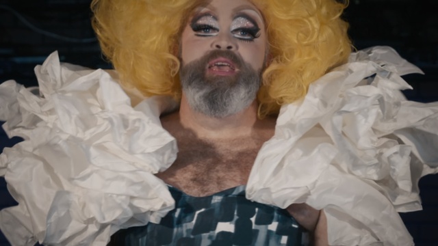 Video Reference: Human, Moustache, Facial hair, Beard, Mouth, Art, Person, Clothes, Holding, Bag, Woman, Plastic, Table, Wrapped, Dressed, Covered, Man, Hot, White, Stuffed, Bed, Sandwich, Dog, Hat, Human face, Face, Human beard, Clothing