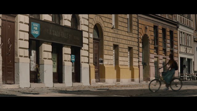 Video Reference: Architecture, Building, Urban area, Town, Facade, Snapshot, Wall, Street, Bicycle, Neighbourhood, Person, Outdoor, Road, Front, Sitting, City, Sidewalk, Sign, Side, Clock, Large, Brick, Bus, Store, Woman, Standing, Walking, Intersection, Stop, Parked, Bench, Man, Train, Riding, Tall, White, Traffic, People, Station, Window, Text, Door